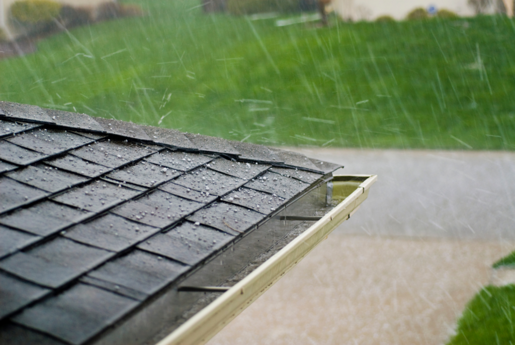 Hailstones pelting a shingled rooftop during a storm, illustrating potential roof damage.