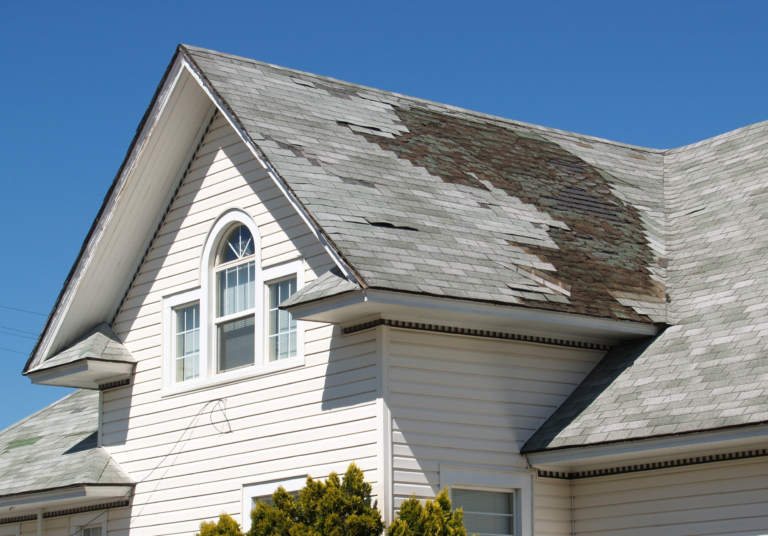 Damaged roof on a house showing signs of wear and missing shingles, questioning home insurance coverage for roof replacement.