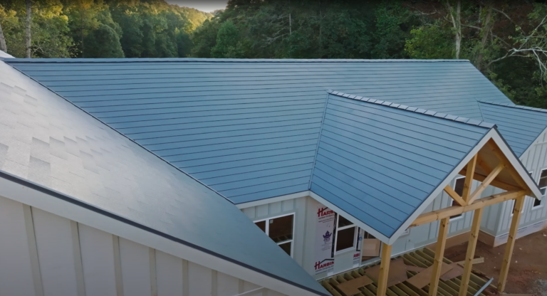 An angled view of a modern Georgia home with a sleek, blue GAF TimberSteel metal roof surrounded by lush green trees, showcasing the durability and contemporary style of the roofing material.