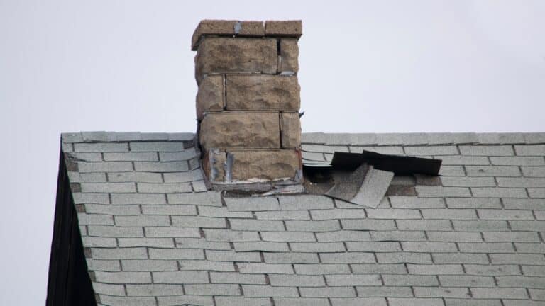 Damaged roof with missing shingles and cracks around a chimney, highlighting the need for emergency roof repair.